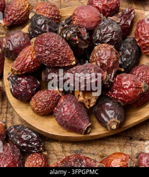 Getrocknete Hagebuttenfrüchte in einem Holzlöffel und auf einem Tisch, Nahaufnahme. Stockfoto