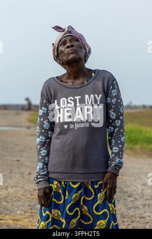 Eine ältere Frau mit Kopftuch schaut nach oben, während sie auf einer Küstenstraße steht, Zentralregion, Elmina, Ghana Stockfoto