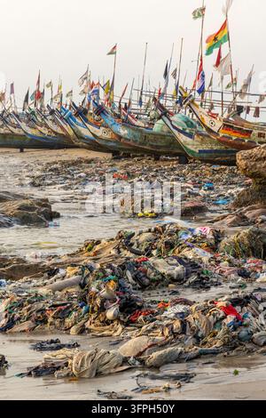 Fischboote, die mit Flaggen geschmückt sind, stehen über einem riesigen Haufen Plastikmüll am Strand, Zentralregion, Cape Coast, Ghana Stockfoto