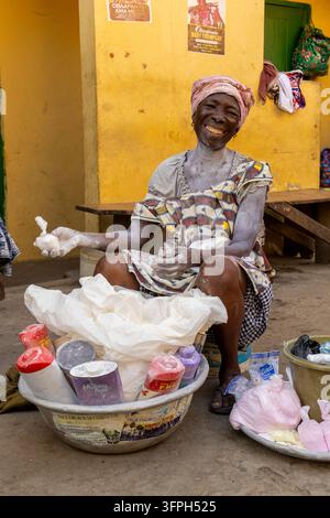 Lächelnde ältere Frau, bedeckt mit weißem Pulver, verkauft Mottenkugeln aus Schüsseln auf einer Straße, Zentralregion, Cape Coast, Ghana Stockfoto