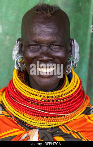 Lächelnde Frau des Turkana-Stammes mit dicken geschichteten Perlenhalsketten und großen silbernen Ohrringen vor einer grünen Wand, Marsabit County, Loiyangalani, Kenia Stockfoto