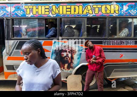 Passagiere in einem farbenfrohen Minibus Matatu namens The Mediator mit einer Frau in einem blauen Oberteil und einem Mann in einer roten Jacke und Mütze davor, Nairobi C Stockfoto