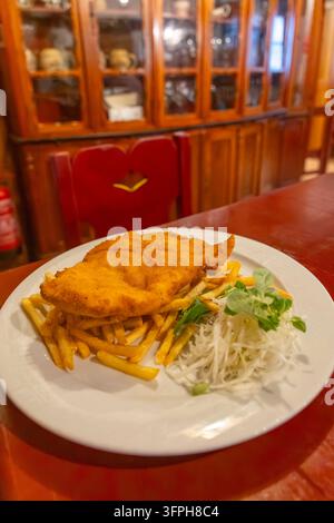 Panierter Schnitzel, Pommes frites und Krautsalat, serviert auf einem Teller in einem rustikalen Restaurant Stockfoto
