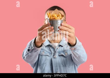 Heißhunger auf Fast Food und ungesunde Ernährung, junger Mann hält einen Becher Pommes frites vor sein Gesicht auf einem rosa Hintergrund Stockfoto