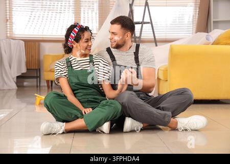 Sanierungs- und Heimwerkerprojekt, glückliches Paar sitzt auf dem Boden und hält sich an den Händen während der Hausrenovierung und Innenrenovierung in einem Wohnzimmer Stockfoto