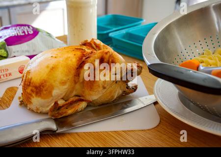 Meal Prep Einfaches Hühnchen Alfredo: ganzes Rotisserie-Huhn mit Schneidewerkzeug und abgetropften Nudeln in der Nudelsieb. Stockfoto