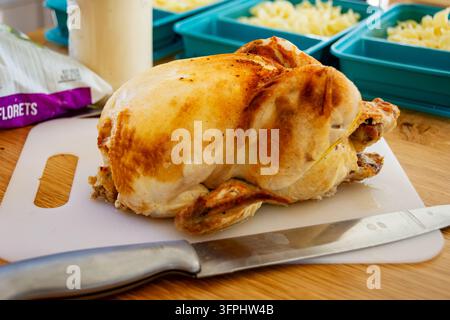 Meal Prep Einfaches Hühnchen Alfredo: goldenes Rotisserie-Hühnchen mit Schneidewerkzeug auf dem Brett mit Nudelblechen bereit. Stockfoto