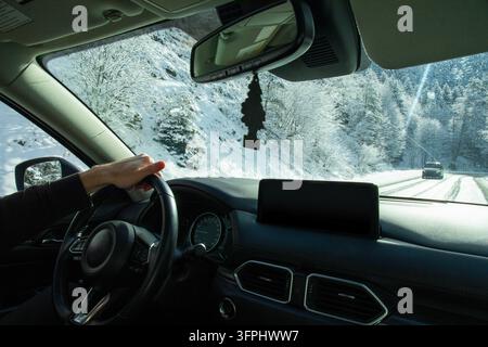 Winterreisen. Fahrerhand am Lenkrad eines Autos, das auf einer schneebedeckten Straße durch einen Winterwald fährt. Winterreisen mit dem Auto Stockfoto