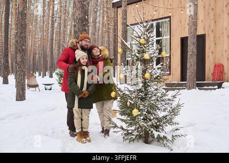 Familie mit Tochter schmückt den Weihnachtsbaum im Winterwald Stockfoto