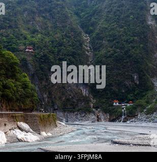 Roter Tempel ragt auf einer steilen grünen Klippe über einem felsigen Flussbett in der Taroko-Schlucht in Taiwan. Stockfoto
