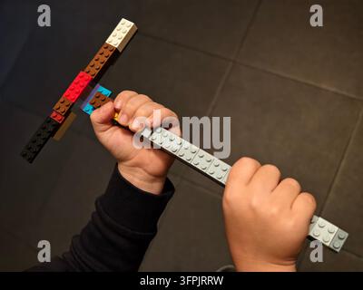 Kinderhände halten eine bunte Spielzeugaxt aus Plastikbausteinen. Stockfoto
