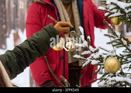 Mann und Frau schmücken einen schneebedeckten Weihnachtsbaum in einem Winterwald Stockfoto