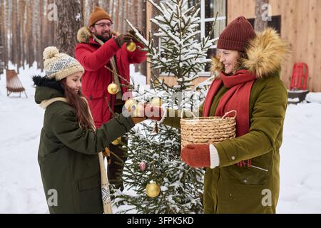 Familie mit Tochter dekoriert den Weihnachtsbaum im Freien im Winter Stockfoto
