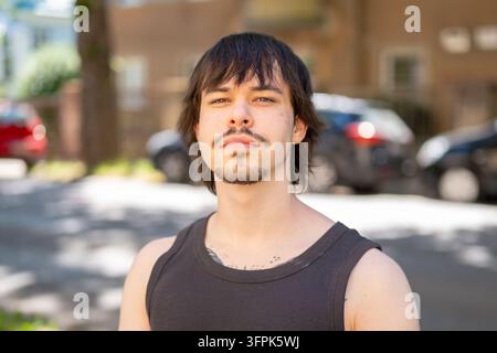 Ein junger Mann mit dunklen Haaren und einem Schnurrbart steht im Freien auf einer verschwommenen Stadtstraße. Stockfoto