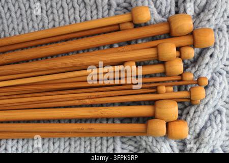 Nahaufnahme von hölzernen Stricknadeln in verschiedenen Größen, die auf einem blauen Kabelmuster-Pullover aus Wolle liegen. Gemütliches handgefertigtes Handarbeiten- und Hobbykonzept. Stockfoto