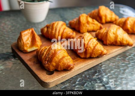 Goldene Buttercroissants ordentlich auf Holzschneidebrett über Glasoberfläche mit sauberem Hintergrund arrangiert. Stockfoto