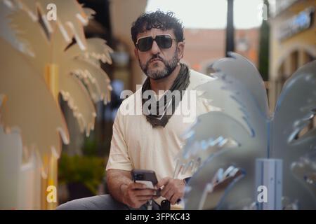 Reifer stilvoller Mann trägt Sonnenbrille und hält Smartphone im Freien Stockfoto