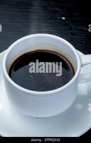 Flat Lay einer weißen Keramiktasse, gefüllt mit frischem schwarzem Kaffee, auf einer Untertasse, die auf einer Teakholzoberfläche platziert ist. Stockfoto