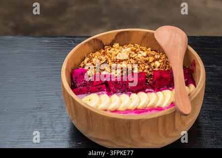 Flachlegung einer gesunden Pitaya-Smoothie-Schale mit Bananen-Granola-Topping, serviert mit Kaffee auf dunklem Holztisch. Stockfoto