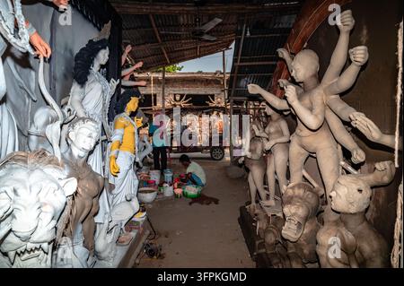 Durga Puja beeinflusst die Wirtschaft, Kultur und Umwelt von Westbengalen erheblich. Die Idole der Göttin Durga werden durch einen traditionellen Tonbildhauprozess gefertigt, der Monate vor dem Festival beginnt. Kunsthandwerker verwenden Alluvialton aus Flussbetten (hier der Jalngi-Fluss), schichten ihn auf eine Strohstruktur, um den Sockel der Statue zu bilden. Die Idole werden dann in Werkstätten innerhalb der Töpferkolonie im Rahmen der Festivalvorbereitungen bemalt. Aufgrund von Zeitdruck und einem Mangel an Kunsthandwerkern beteiligen sich alle in der Töpferkolonie – einschließlich verheirateter Frauen und Kinder, die normalerweise nicht an solchen Aktivitäten teilnehmen Stockfoto