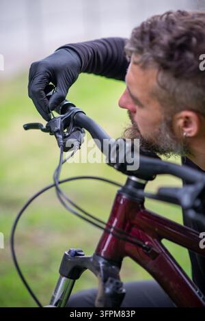 Nahaufnahme eines bärtigen Mannes mit schwarzen Handschuhen, der im Freien einen Fahrradbremsehebel einstellt. Stockfoto