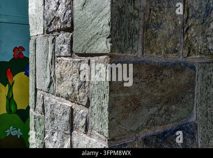 Ein natürlicher quadratischer und rechteckiger Steinbelag mit graugrünen Tönen und gespaltener Oberfläche, der an einer Außenwand oder Ecke installiert ist. Stockfoto