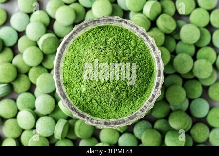 Zerkleinerte Chlorella oder Spirulina in einem Glasbecher vor einem Tablet-Hintergrund. Oberblick. Stockfoto