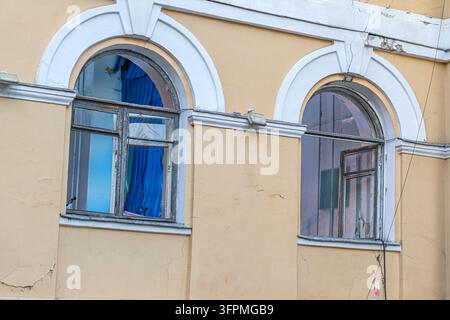 Vintage gewölbte Fenster in städtischem Verfall, die eine gealterte Putzwand mit abblätternder Farbe zeigen, weiches Tageslicht wirft Schatten, die die Texturen hervorheben, kontrastierendes Licht Stockfoto