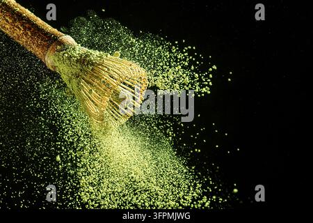 Bambus-Schnürer mit fliegendem Matcha-Teepulver auf schwarzem Hintergrund. Stockfoto
