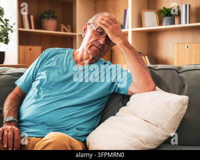 Älterer Mann sitzt zu Hause auf dem Sofa, leidet unter Kopfschmerzen, Angst und Stress, fühlt sich müde und sorgt sich um seine Gesundheit. Stockfoto