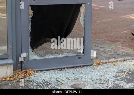 Nahaufnahme einer zersplitterten Glastür mit zerbrochenem Fenster und Glasscherben, die auf dem Bürgersteig verstreut sind Stockfoto