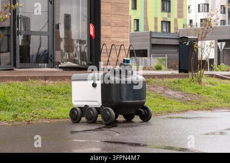 Moderner automatisierter Lieferroboter steht draußen und wartet bei regnerischem Wetter auf eine Bestellung. Modernes Konzept der Lieferung von Waren an den Kunden. Stockfoto