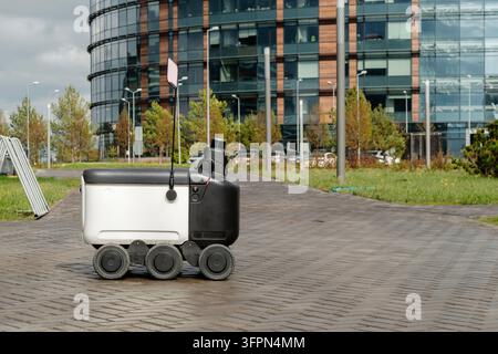 Moderner automatisierter Lieferroboter steht draußen und wartet bei regnerischem Wetter auf eine Bestellung. Modernes Konzept der Lieferung von Waren an den Kunden. Stockfoto