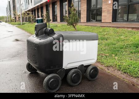 Moderner automatisierter Lieferroboter steht draußen und wartet bei regnerischem Wetter auf eine Bestellung. Modernes Konzept der Lieferung von Waren an den Kunden. Stockfoto