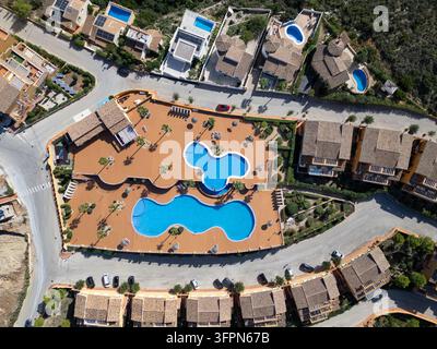 Luftbild von zwei großen, einzigartig geformten Schwimmbädern, umgeben von gefliesten Terrassen, Palmen und Villen im mediterranen Stil in Moraira, Valencia Stockfoto
