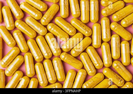 Glänzende gelbe Nahrungsergänzungsmittel-Kapseln füllen rosa Hintergrund in Top-Down-Ansicht, lebendiges Muster für Wellness-Marken-Design, Apothekenwerbung oder Blogs. Stockfoto