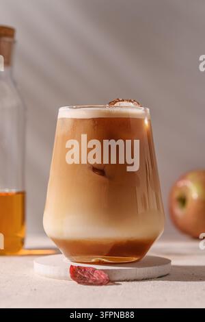 Eisgekühlter Apfel-Latte mit geschichteter Milch und Kaffee steht auf einem Untersetzer, Sonnenlicht hebt die Textur hervor und erweckt eine erfrischende Herbststimmung. Stockfoto