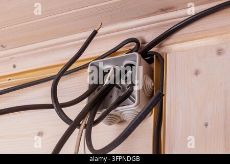 Offener Anschlusskasten mit freiliegenden Kabeln vor einer Holzwand betont den Prozess der elektrischen Installation vor dem Anschließen und Isolieren. Stockfoto