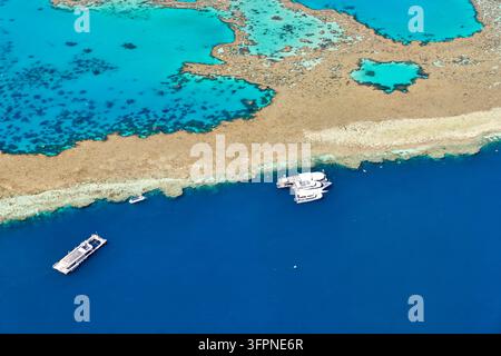 Luftaufnahme eines Riffrandes in Queensland mit festgemachten Katamaranen, einem kleinen Boot und einer schwimmenden Plattform neben tiefblauem Ozean und flachen Lagunen Stockfoto