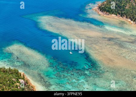 Luftaufnahme eines Segelkatamarans in einem tiefblauen Kanal zwischen Saumkorallenriffen und zwei bewaldeten Inseln vor der Küste Australiens Stockfoto
