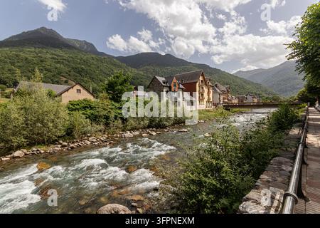 Bossost, Spanien. Malerischer Blick auf den schnell fließenden Garonne-Fluss mit Steinen und Weißwasser, der durch die Bergstadt mit traditionellen Schieferdächern fließt Stockfoto