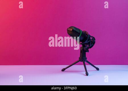 Studiumikrofon auf Stativ steht vor einem lebhaften rosa Hintergrund und bildet ein klares, modernes Setup für Podcasts, Streaming und Audioinhalte Stockfoto