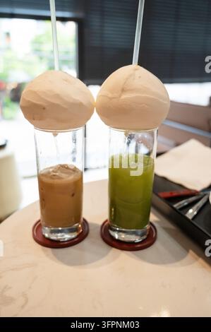 Kreative Präsentation von Eiskaffee und Matcha-Eis in hohen Gläsern, in die Kokoswasser aus der Kokosnuss fließt, serviert in einem modernen Café in Vietnam Stockfoto
