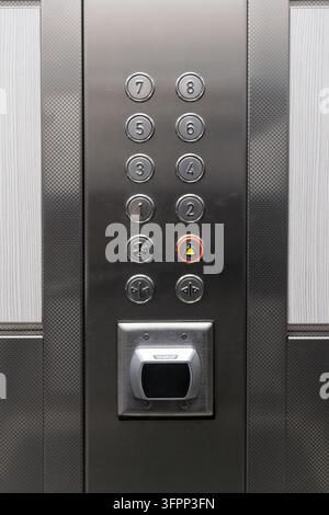 Moderne Aufzugsteuerung mit Edelstahl-Finish, nummerierten Stockwerktasten, beleuchtetem Alarmknopf und Schlüsselkartenleser. Stockfoto