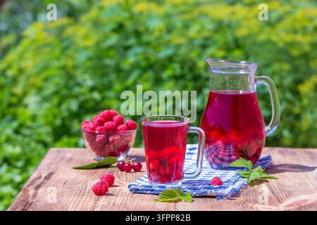 Rotes Kompott mit Kirsche, Erdbeere, Stachelbeere und Himbeere auf Holztablett in der Natur, im Freien, Nahaufnahme Stockfoto