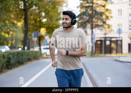 Junger Mann trainiert aktiv und genießt Musik während eines Outdoor-Laufs in der Stadt, fördert urbanes Wohlbefinden, gesunden Lebensstil und Technologieintegration in Fitnessroutinen Stockfoto