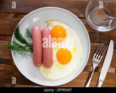Es gibt frisch gekochtes Frühstück auf dem Teller – Rührei mit ganz gebratener Schweinehähnchensauerwurst. Traditionelles europäisches spanisches Frühstück ist gebraten Stockfoto