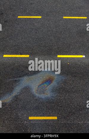 Hohe Ansicht eines regenbogenfarbenen Ölflecks auf dunklem Asphalt neben gelb markierten Fahrbahnen, ein abstraktes Detail der Verschmutzung in einem Fährhafen in Tallinn Stockfoto