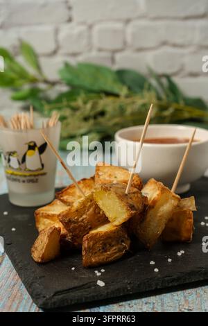 Goldbraun geröstete Patatas Bravas, ein beliebtes spanisches Tapas-Gericht, präsentiert auf einem dunklen Schiefer mit einer Beilage aus Dippingsauce Stockfoto