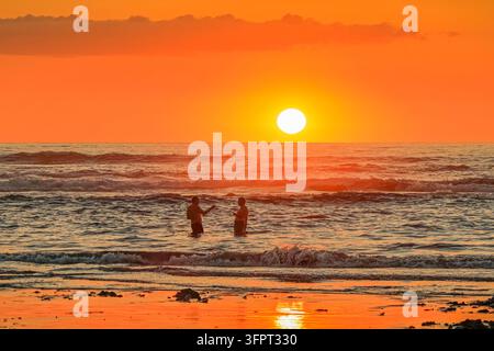 Zwei männliche Freunde genießen Bier bei Sonnenuntergang am Guiones-Strand in der Nähe von Garza, Guiones, Nosara, Guancaste, Costa Rica Stockfoto